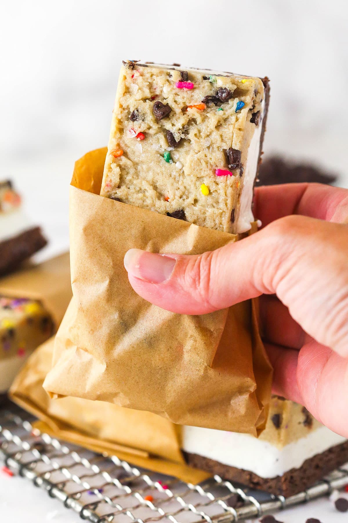 A hand holding a brownie cookie dough ice cream sandwich
